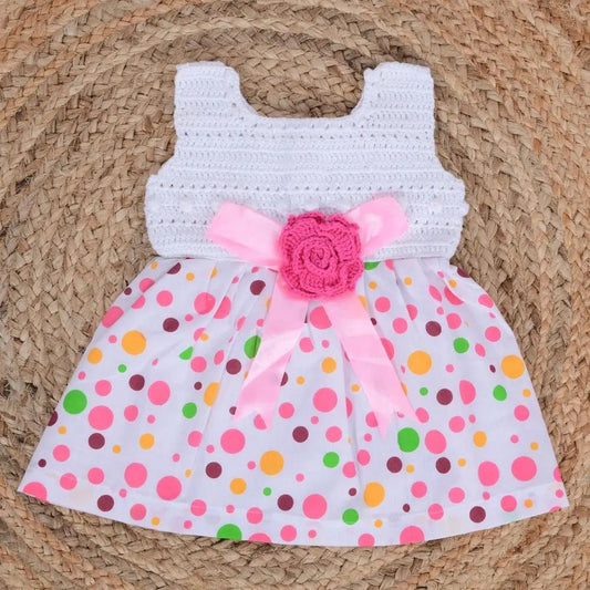 Crocheted dress with colorful polka dot skirt and pink flower on a woven surface