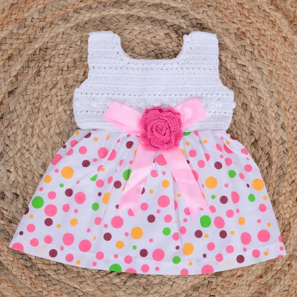 Crocheted dress with colorful polka dot skirt and pink flower on a woven surface