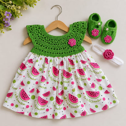 Green crochet and watermelon-print frock laid flat with matching green floral shoes and a white flower headband.